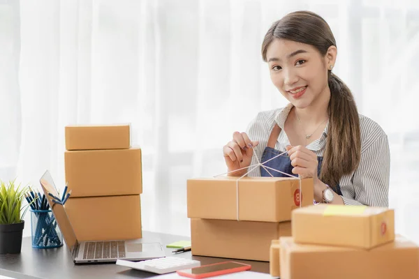 beautiful asian woman working at home selling online with yellow box and laptop on taking name orders from customers sme business concept parcel delivery