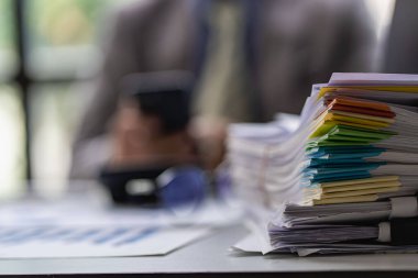 Finans sektöründe çalışan bir iş adamı. Masa başı işindeki kağıt yığınının üzerinde bitmemiş kağıtlar var.