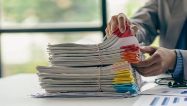 Finans sektöründe çalışan bir iş adamı. Masa başı işindeki kağıt yığınının üzerinde bitmemiş kağıtlar var.
