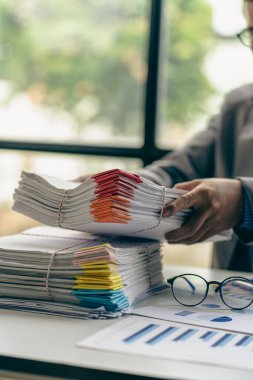 Finans sektöründe çalışan bir iş adamı. Masa başı işindeki kağıt yığınının üzerinde bitmemiş kağıtlar var.