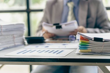 Finans sektöründe çalışan bir iş adamı. Masa başı işindeki kağıt yığınının üzerinde bitmemiş kağıtlar var.