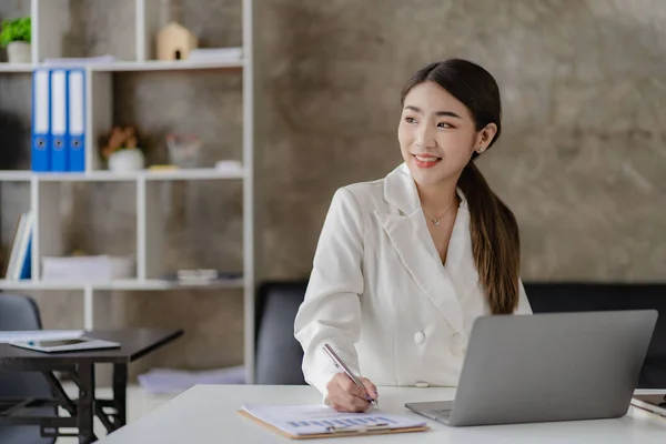 Smiling Asian businesswoman working on laptop in modern office, accountant, concept, finance, expert, analysis, business report, graph, financial chart, economy, corporate, banking, market research.