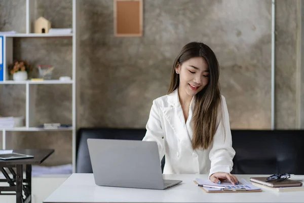Smiling Asian businesswoman working on laptop in modern office, accountant, concept, finance, expert, analysis, business report, graph, financial chart, economy, corporate, banking, market research.