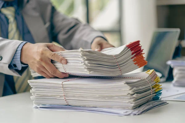 Businessman working in finance with pile of unfinished papers on the desk business paper pile