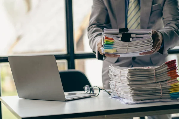 Businessman working in finance with pile of unfinished papers on the desk business paper pile