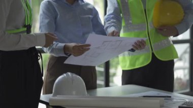 İnşaat inşaatçıları, mimarlar, mühendisler ve müfettişlerle inşaat toplantıları. Ofisteki çeşitli planlama planlarına bakıyorlardı. 4K stok video klibi.