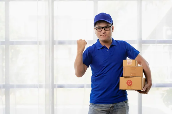 Asian man in blue t-shirt wearing glasses holding yellow box white background delivery concept