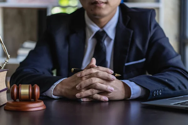 A law firm with an Asian male lawyer working at a table with hammers and scales, the goddess of justice.