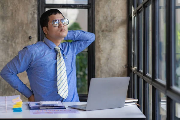 Young Asian businessman has pain from sitting at work looking at laptop screen for a long time, office syndrome concept.
