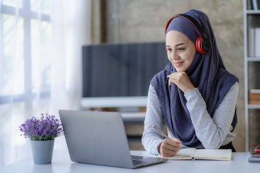 Başörtüsü takan Müslüman kız öğrenciler çevrimiçi çevrimiçi uzak çevrimiçi toplantılarda dizüstü bilgisayar ve kulaklıklarla çalışıyorlar..