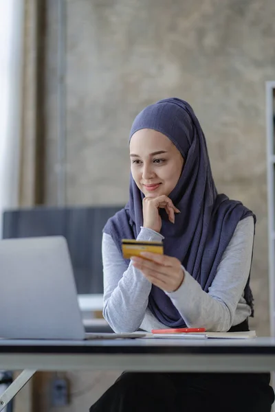 Muslim woman wearing hijab is buying online with credit card at home. with using a laptop computer and doing online transactions