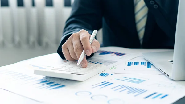 Businessman holding pen pointing to graph while analyzing financial paper graph and on desk at office