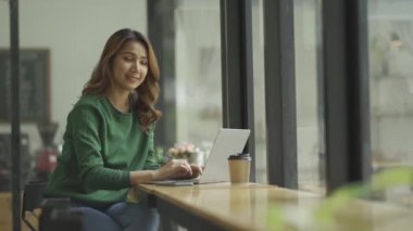 Güzel ve zeki Asyalı bir kadın, mutlu bir ruh hali ve kahvede dizüstü bilgisayar kullanan, kendinden emin ve 4K kahve dükkanında dizüstü bilgisayarda yazan çekici bir kadın.