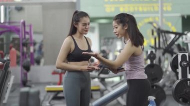 Spor salonunda egzersiz öncesi konuşan iki Asyalı kız spor salonunda. Makinanın sırtındaki kaslar için doğru egzersiz fikirleri.