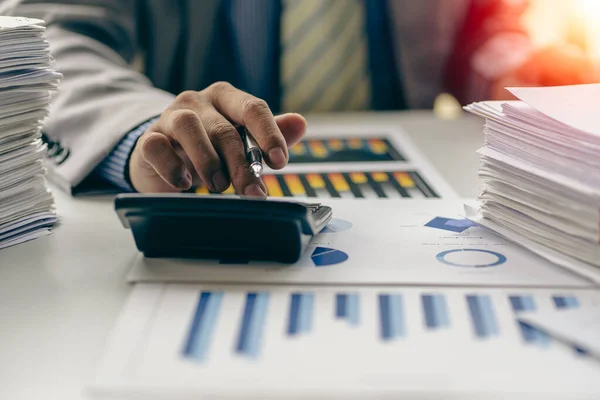 Businessman presses calculator to calculate income tax and corporate income in private office, finance, accounting, market investor statistics graph.