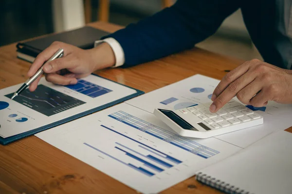 Businessman presses calculator to calculate income tax and corporate income in private office, finance, accounting, market investor statistics graph.