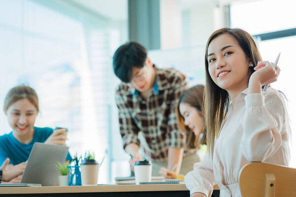 Asian creative teams sit and work together to share inspirational creativity in a workshop. Young modern businessmen are meeting with graph paper and laptop in the workplace.