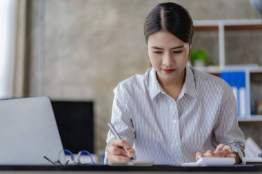 Modern ofiste dizüstü bilgisayar kullanan Asyalı bir kadın emlak yatırım vergisi ve finans sistemi kavramları hakkında bir hesap analizi raporu hazırlıyor