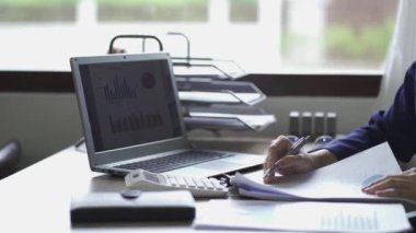 Genç Asyalı iş kadını, gelir vergisi ve kurumsal geliri özel ofiste hesaplamak için hesap makinesine baskı yapıyor. Maliye, muhasebe, pazarlamacının istatistiksel grafiği.