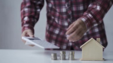 Para tasarrufu konsepti. Genç bir adam yanında hesap makinesi olan bir evin kavanozuna bozuk para koyar..