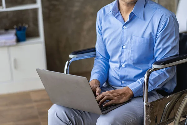 Asian man sitting in a wheelchair and work on the computer at home The concept of technology for convenience