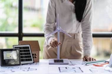 Ofiste lapotp üzerinde çalışan Asyalı genç bir mimar. Ahşap masa üzerinde çalışmak, yel değirmenleriyle resim yapmak, yenilenebilir rüzgar evi modelleri tasarlamak. ve güneş ışığı.