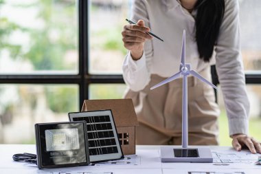 Ofiste lapotp üzerinde çalışan Asyalı genç bir mimar. Ahşap masa üzerinde çalışmak, yel değirmenleriyle resim yapmak, yenilenebilir rüzgar evi modelleri tasarlamak. ve güneş ışığı.