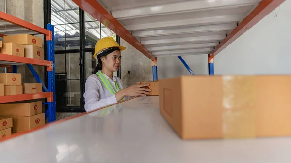 Asian Caucasian woman warehouse worker checking parcel using tablet in large distribution center, delivery concept.