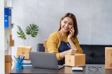 KOBİ girişimcisi veya bağımsız yaşam konsepti, genç kadın, küçük işletme sahibi, evden online alışveriş, arka planda paketlenmiş ürünleri olan dizüstü bilgisayarlı müşterilerin siparişlerini onayla.