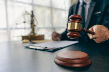 Sözleşme belgeleri ve altın tanrıça terazileri üzerinde çalışan bir avukat. Masasında çekiçle tavsiye, adalet ve hukuk müşaviri imajı sunan bir avukat..
