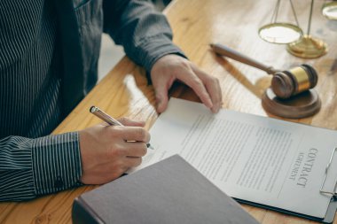 Sözleşme belgeleri ve altın tanrıça terazileri üzerinde çalışan bir avukat. Masasında çekiçle tavsiye, adalet ve hukuk müşaviri imajı sunan bir avukat..