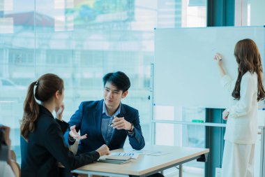 Yeni nesil girişimcilerin genç erkek ve bayanları. Asyalı kadın çalışanların memnuniyetine yönelik bir proje sunuyorum. Ofiste yaratıcı bir iş yerinde işbirliği yapın..