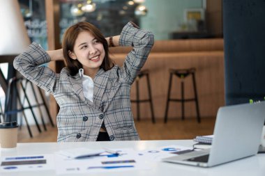 Ahşap masa, vergi, muhasebe, istatistiksel raporlar ve finansal grafikli analitik araştırma kavramları üzerinde matematik finansmanı için hesap makinesi ve dizüstü bilgisayar kullanan Asyalı kadın.