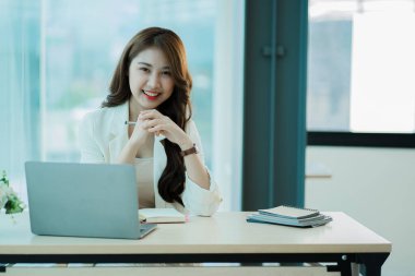 Ahşap masa, vergi, muhasebe, istatistiksel raporlar ve finansal grafikli analitik araştırma kavramları üzerinde matematik finansmanı için hesap makinesi ve dizüstü bilgisayar kullanan Asyalı kadın.