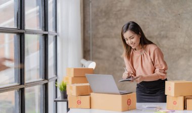 Çevrimiçi KOBİ iş ve dağıtım konsepti, gülümseyen kız, güzel sahibi, Asyalı serbest çalışan, online alışveriş KOBİ işi evdeki masada paket kutularıyla dizüstü bilgisayarda çalışıyor..