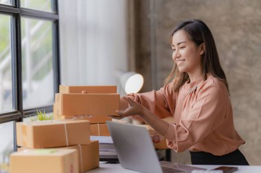 Çevrimiçi KOBİ iş ve dağıtım konsepti, gülümseyen kız, güzel sahibi, Asyalı serbest çalışan, online alışveriş KOBİ işi evdeki masada paket kutularıyla dizüstü bilgisayarda çalışıyor..
