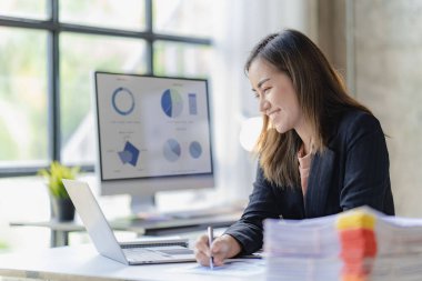 İş yerinde dosyası ya da belgesi olan Asyalı bir iş kadını iş bilgisayarı hesap makinası finans muhasebecisi ile para hesaplıyor.