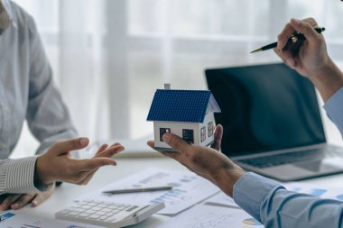 Bir emlakçı ya da aracı müşterilerle görüşür, emlak alımı ve sigorta sözleşmesini tartışır, ek iş olarak da ev örnekleri sunar..