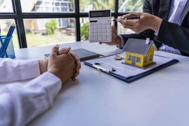 Bir emlakçı ya da aracı müşterilerle görüşür, emlak alımı ve sigorta sözleşmesini tartışır, ek iş olarak da ev örnekleri sunar..