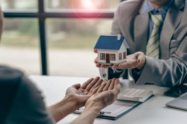 Bir emlakçı ya da aracı müşterilerle görüşür, emlak alımı ve sigorta sözleşmesini tartışır, ek iş olarak da ev örnekleri sunar..