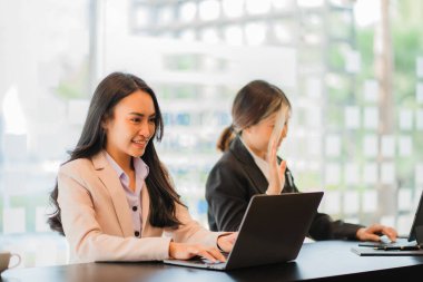 Küçük bir iş için ofiste birlikte çalışan iki genç kadın dizüstü bilgisayarlarıyla oturup rapor ya da belge okuyorlar..