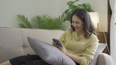 Kanepede akıllı telefon çalan Asyalı bir kadın. Güzel bir kadın. Evde akıllı telefondan oyun oynuyor.