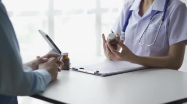 Kadın bir doktor, erkek hastasına masanın önünde oturmasını ve ilaç almasını tavsiye eder..