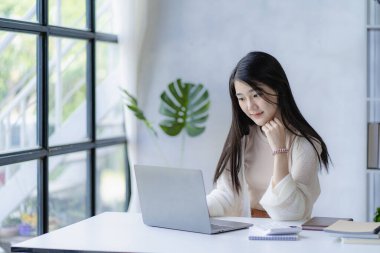 Güzel genç Asyalı muhasebeci evde dizüstü bilgisayarla ve finansal grafikle çalışıyor..