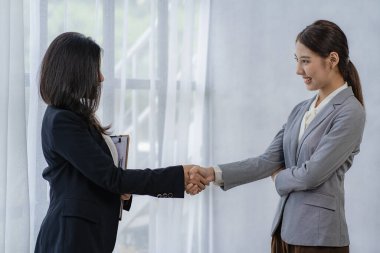 İki Asyalı iş kadını modern bir şirkette buluşup el sıkışıyor. Yandan bakıldığında İşbirliği konsepti ve selamlar