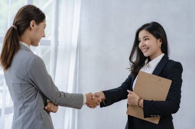 İki Asyalı iş kadını modern bir şirkette buluşup el sıkışıyor. Yandan bakıldığında İşbirliği konsepti ve selamlar