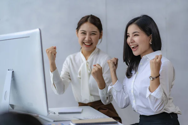 Two Asian business women excited by their computers at their desks. independent woman reading financial graph chart plan analysis calculation office market data