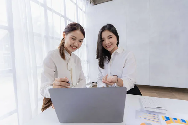 Two Asian businesswomen attending two Asian business partners discuss the financial and company planning graph during a budget meeting.