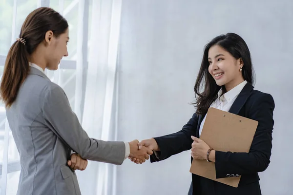 Two Asian business women meet in a modern company and shake hands. at the side view Cooperation concept and greetings