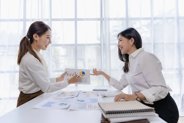 Two Asian businesswomen attending two Asian business partners discuss the financial and company planning graph during a budget meeting.